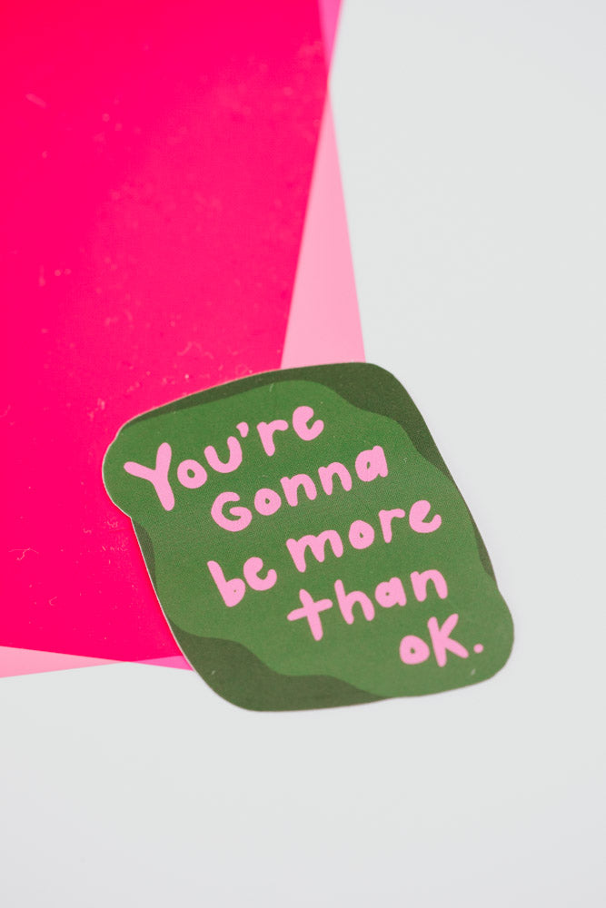 A colorful sticker with the phrase "You're gonna be more than okay" in bold, uplifting letters.