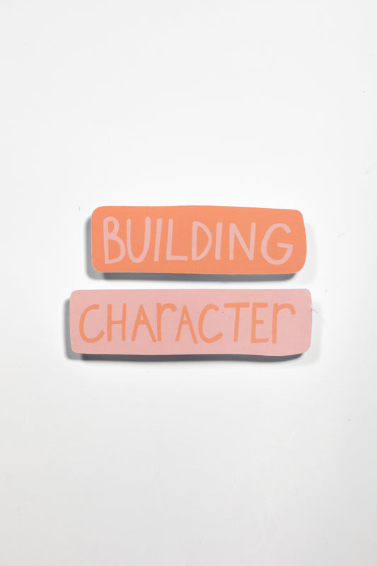 Close-up product shot of the two-piece 'Building Character' sticker in peach and pink tones against a white background, showing subtle shadow detail