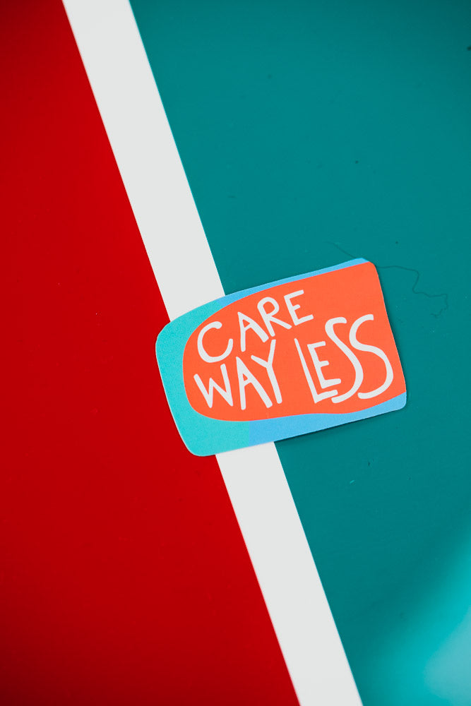 A rectangular sticker with 'Care Way Less' text in white letters on a coral-colored background with turquoise border, photographed against a diagonal split background of red and teal