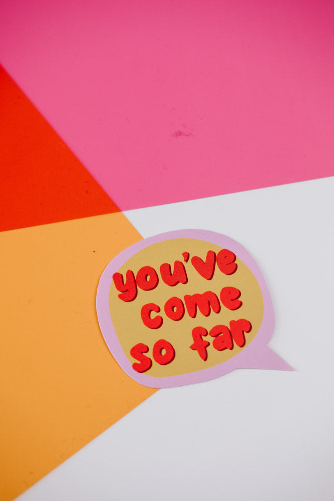 A single speech bubble sticker placed on a geometric background divided into sections of pink, red, orange, and white colors. The sticker has a pink border, yellow background, and red bubble letters reading 'you've come so far