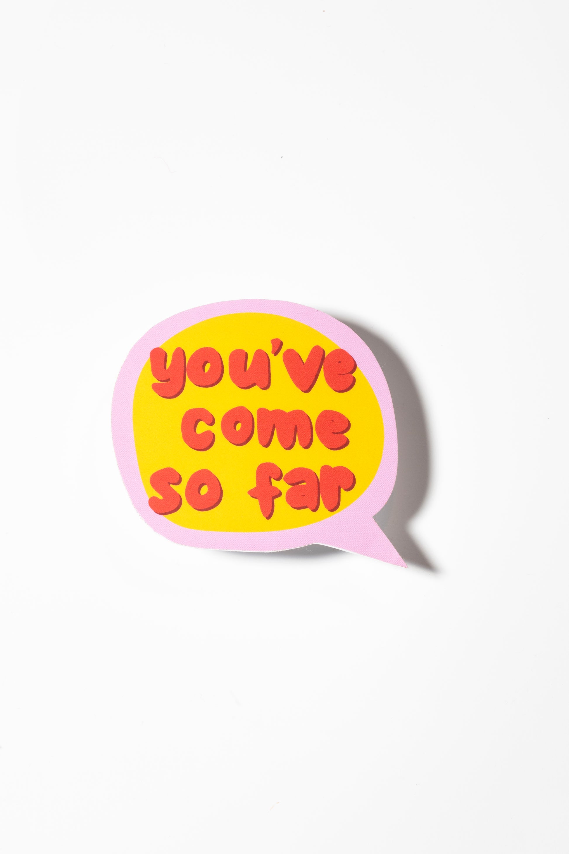 A single speech bubble sticker photographed against a plain white background, casting a subtle shadow. The sticker features a pink border, yellow background, and red bubble letters reading 'you've come so far'. The sticker is positioned centrally in the frame