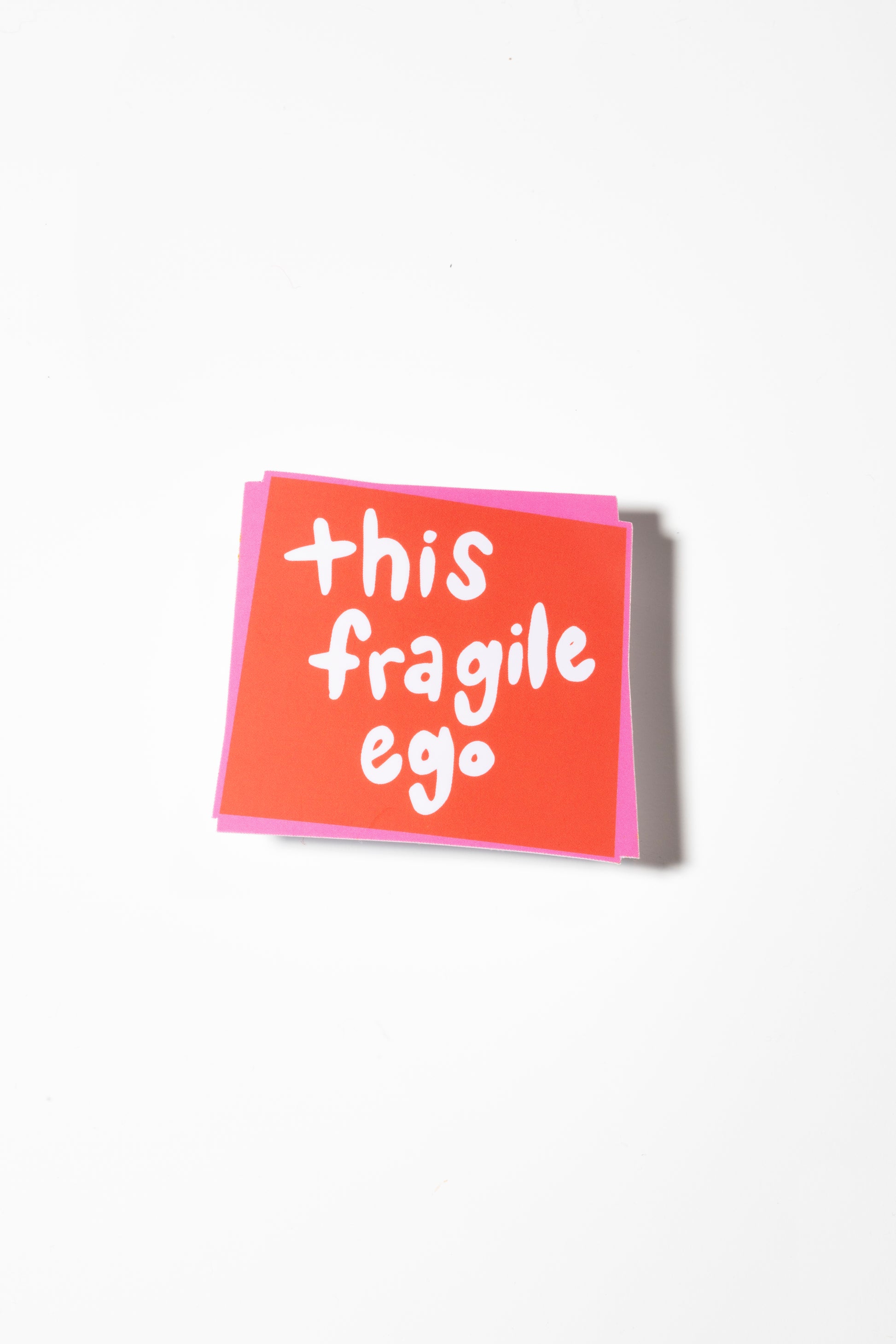 Red square sticker that reads "this fragile ego" in white handwritten letters.