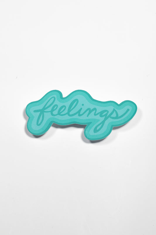 A close-up shot of the turquoise 'feelings' sticker on a white background, showing its curved script lettering and subtle shadow detail"