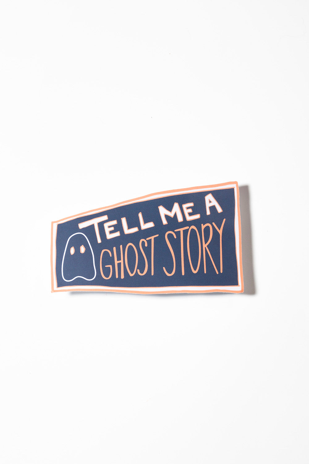 Blue geometric sticker that reads "tell me a ghost story" in pink and white shot on a white background.