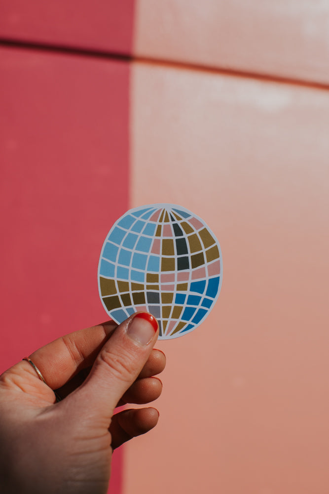 Hand holding a disco ball sticker against a pink and red background.