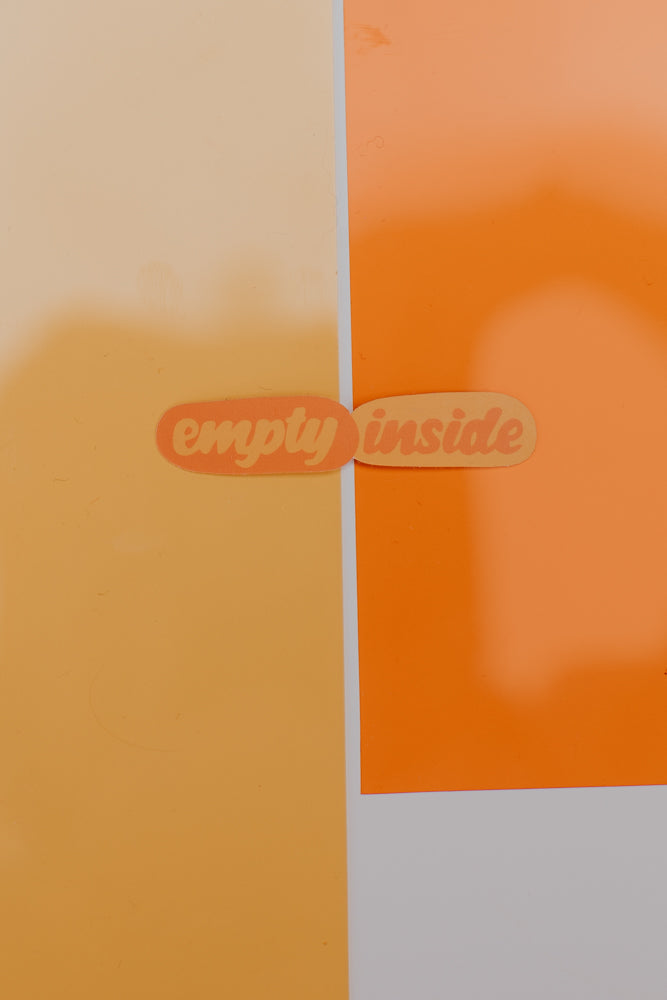 A close-up image of the "empty inside" sticker, which is displayed against a bright orange and yellow background.